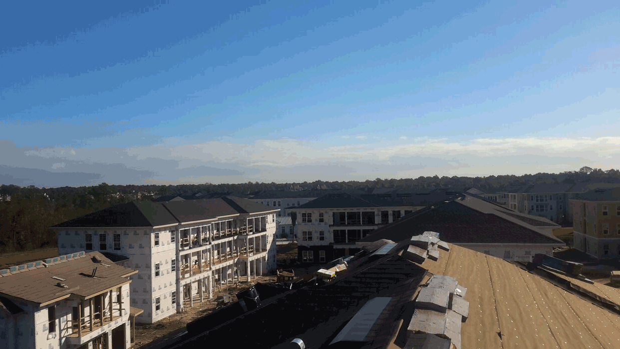 Aerial view of active multifamily roofing construction, with apartment buildings and unfinished rooftops